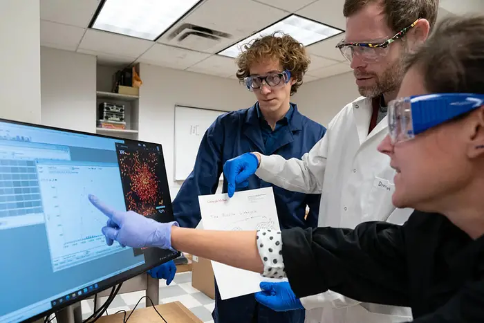 Three scientists huddled around a monitor, discussing AI-driven data on the screen and a physical report.