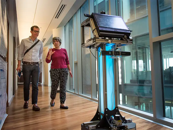 Two people following an AI robot with a touch screen.