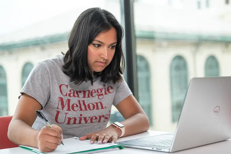 CMU undergraduate student, taking notes while looking at her laptop.